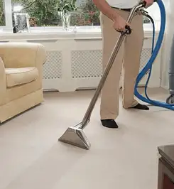 Professional carpet cleaner using a hot-water extraction wand and hose machine in a living room in Chattanooga, TN.